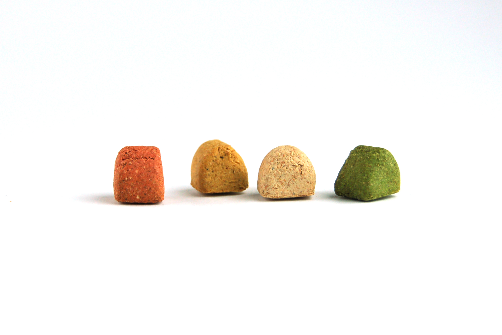 Vier bunte Tierfutterstücke; rot, braun, beige, grün; pyramidenförmig; minimalistische Darstellung.