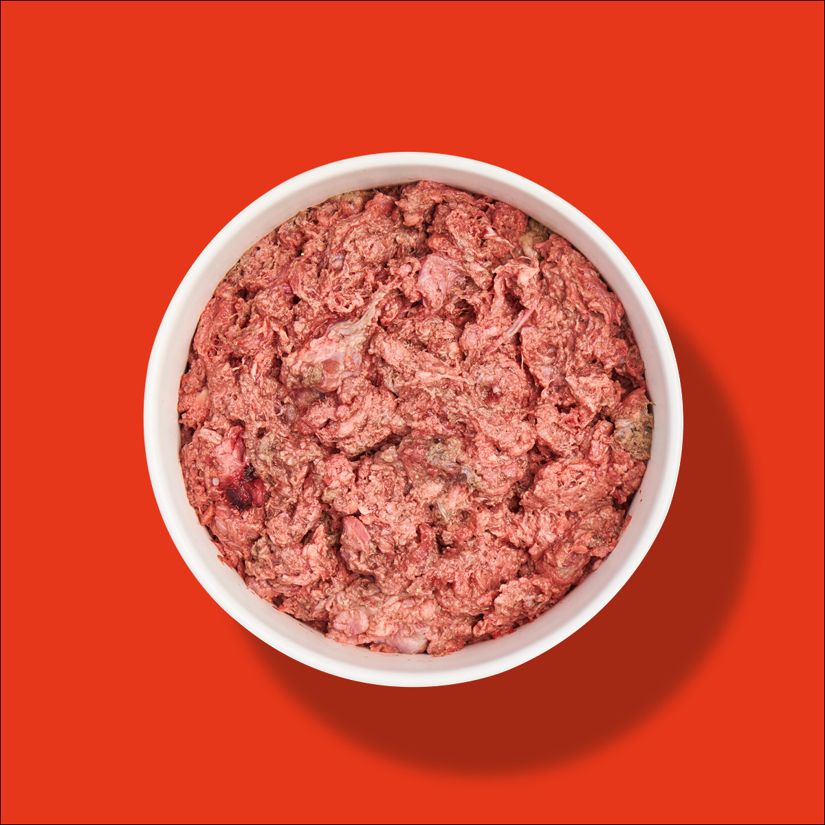 Nutriment Compact LEFZEN / MAULFLEISCH Weiße Schüssel mit rohem, zerkleinertem Maulfleisch vor rotem Hintergrund