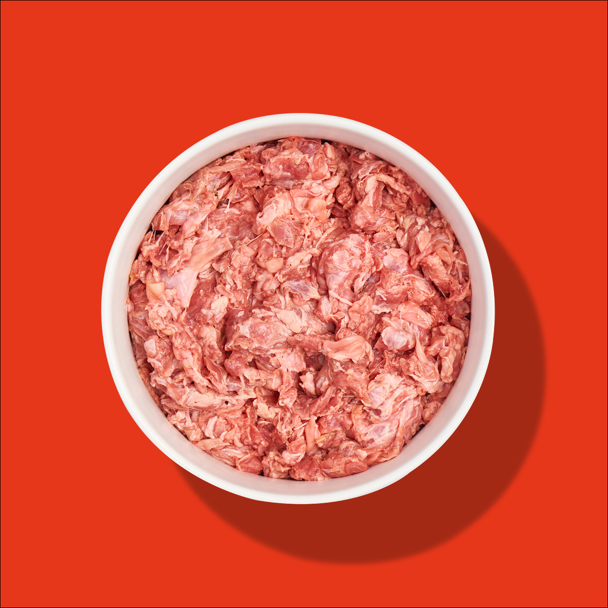 Nutriment Compact SCHLUND Weiße Schüssel mit rohem, gehacktem Fleisch vor rotem Hintergrund