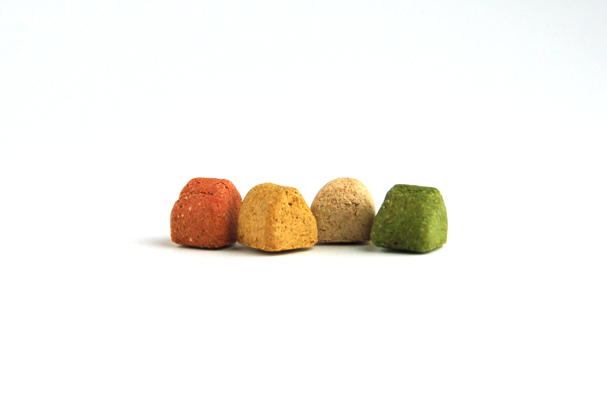 Vier bunte Katzenleckerlis, pyramidenförmig, in den Farben Rot, Gelb, Beige, Grün, auf weißem Hintergrund.