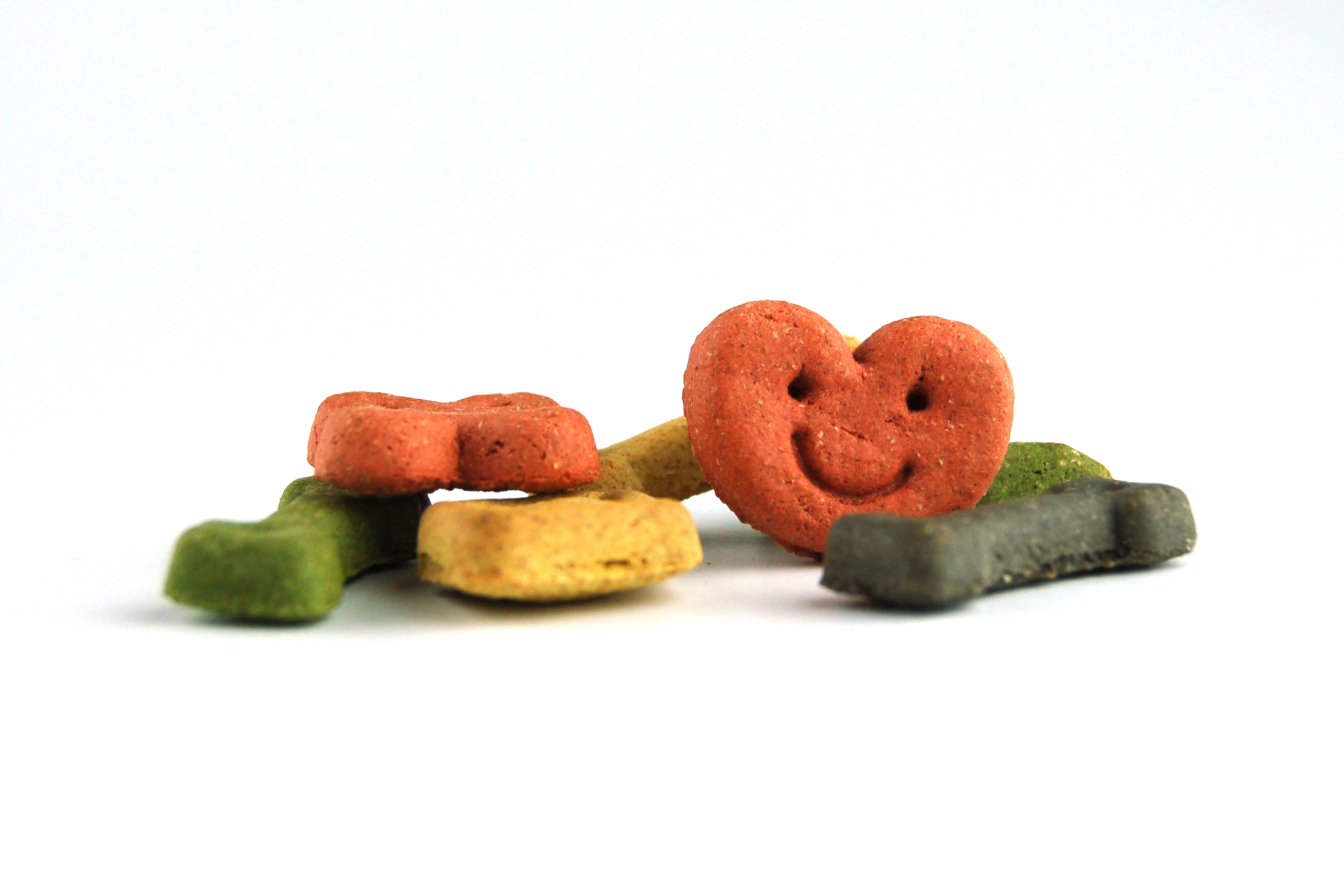 Hundekekse, bunte Farben, Knochen- und Herzform, Gesichtsmotiv auf rotem Herz, grün, gelb, rosa und grau.