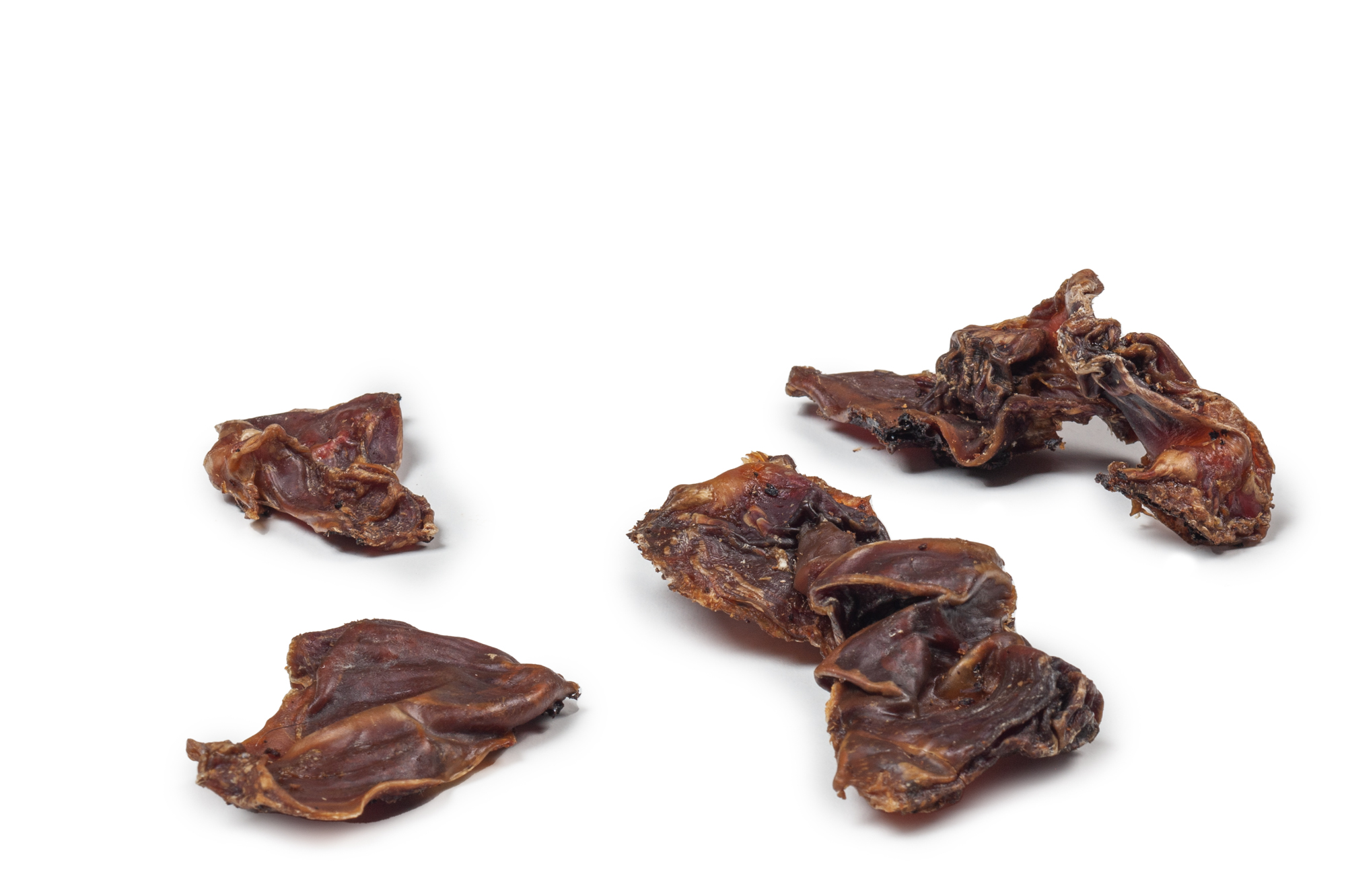 DIBO Hähnchen-Mägen, 100g-Beutel Mehrere getrocknete Hähnchenmägen auf weißem Hintergrund verteilt
