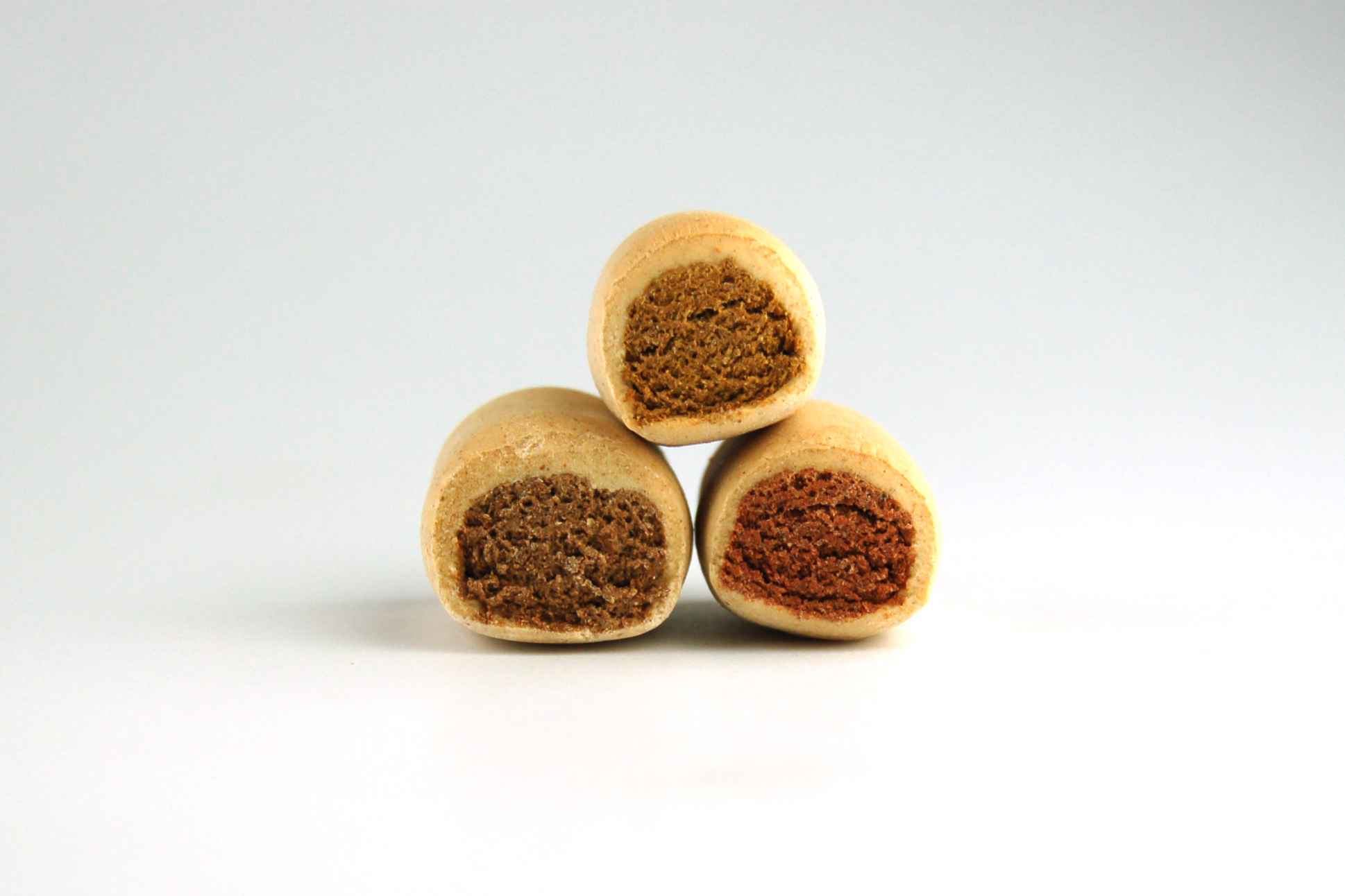 Dreierlei Hundekekse, beige Kruste, unterschiedliche Füllungen in braun, dunkelbraun und rotbraun, gestapelt.