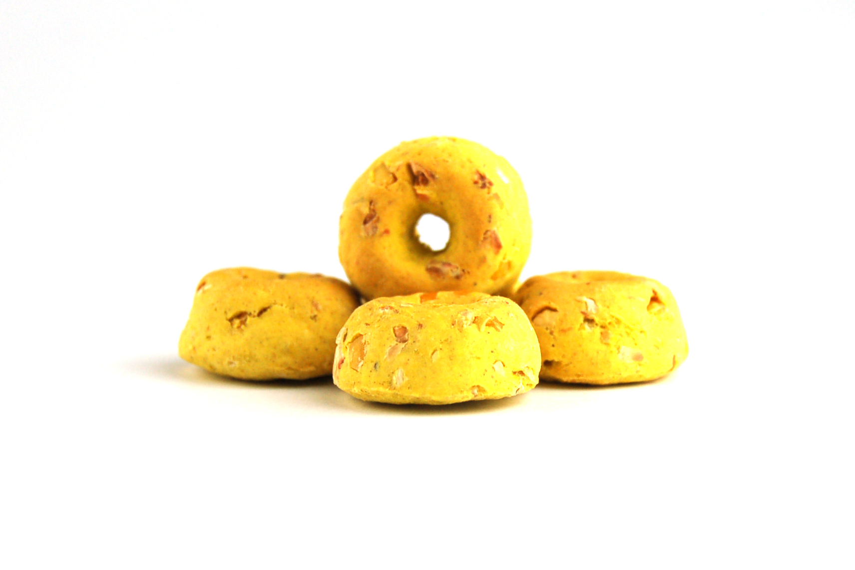 Fünf gelbe runde Hundekekse, donutförmig, mit sichtbaren kleinen Stückchen, auf weißem Hintergrund.